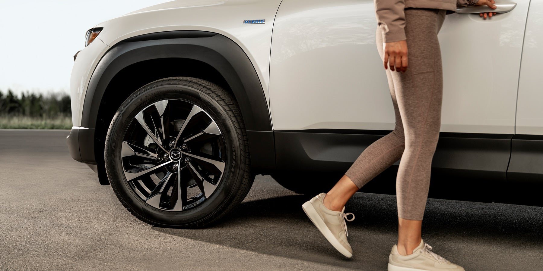 A white SUV driving down a road with green trees.